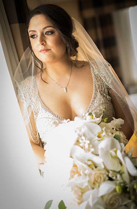 Bride looking out her window while holding her white bouquet. 