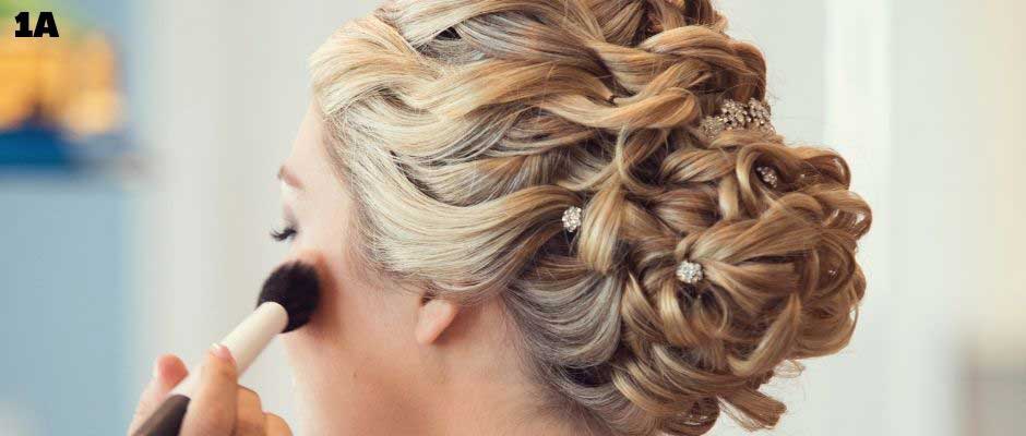 Bride showcases detailed twisted low bun hairstyle with crystal pins as she gets her makeup done.