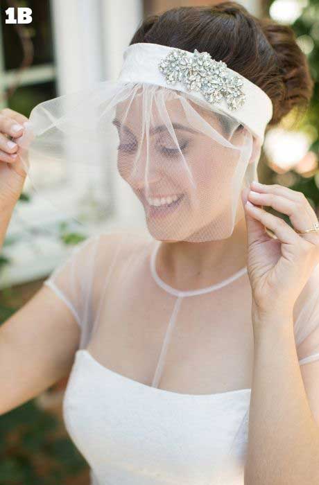 Bride models her birdcage wedding veil with crystal headpiece and low bun.