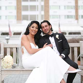 Bride and Groom sitting on a wooden bench outside the Garden City Hotel.