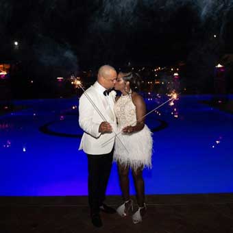 A night shot of a bride and groom kissing and holding sparklers in front of the pool at Crestwood.