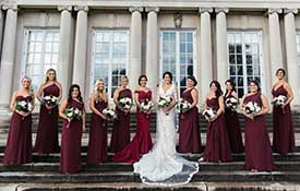 Bride and Bridesmaids in burgundy dresses standing outside on steps.
