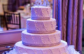 Four tiered wedding cake in room with purple uplighting.