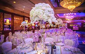Table set with white flower centerpieces in room with purple uplighting.