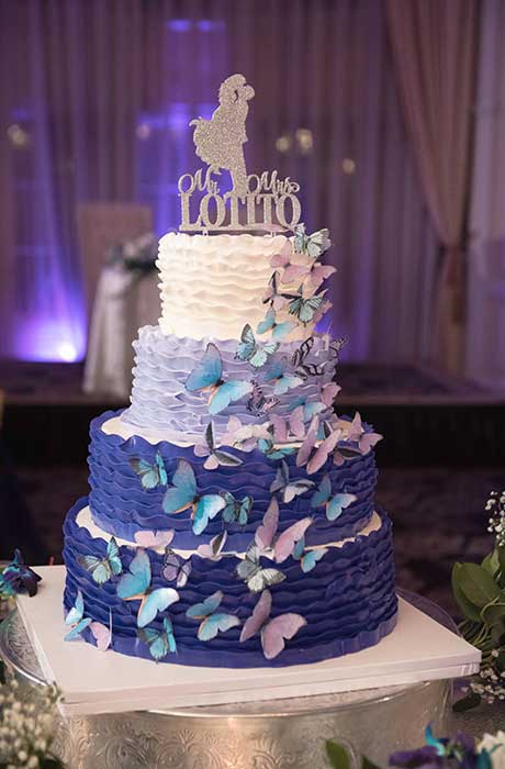 Blue and white 4-tier wedding cake with butterflies cascading on one side of the cake.