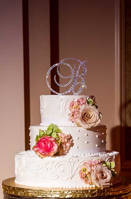 Three tier wedding cake with a single pink or blush flowers on each tier of the cake.