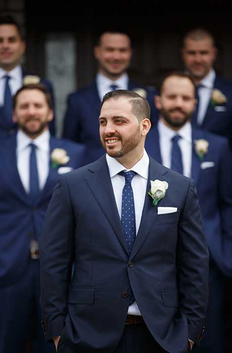 Groom wearing a dark blue suit standing in front of his groomsmen’s.