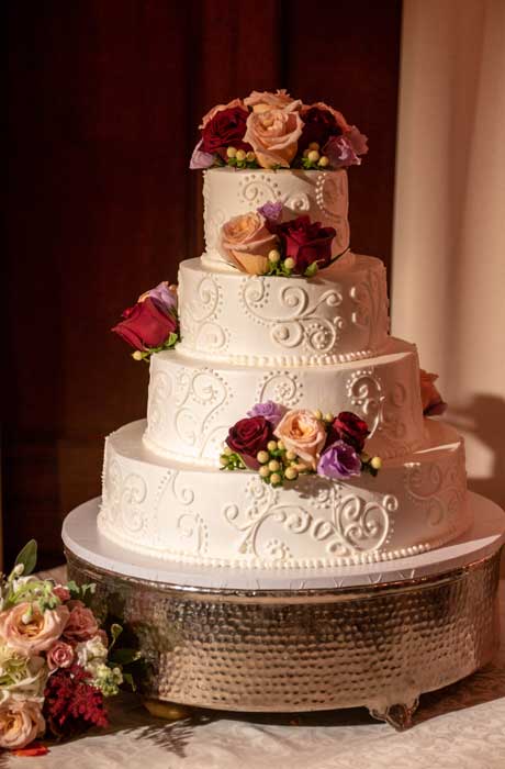 Photo of wedding cake decorated with a few red and white flowers. 
