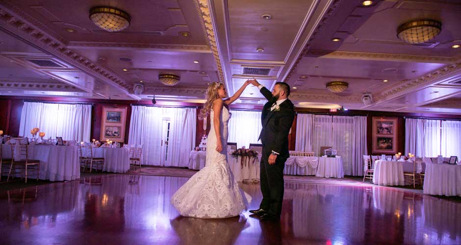 Bride and Groom posing in their reception ballroom with purple uplighting. 