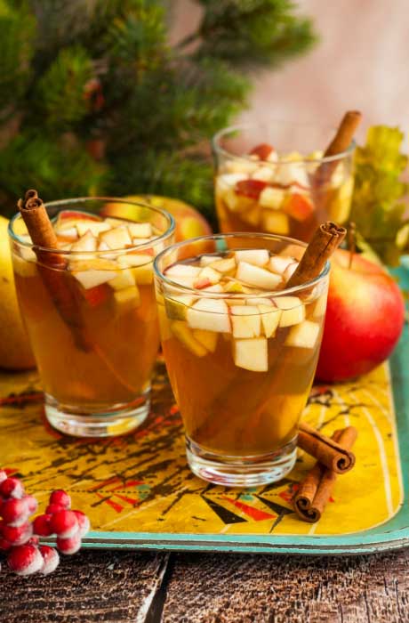 Three cider drinks with apple pieces and a cinnamon stick. 