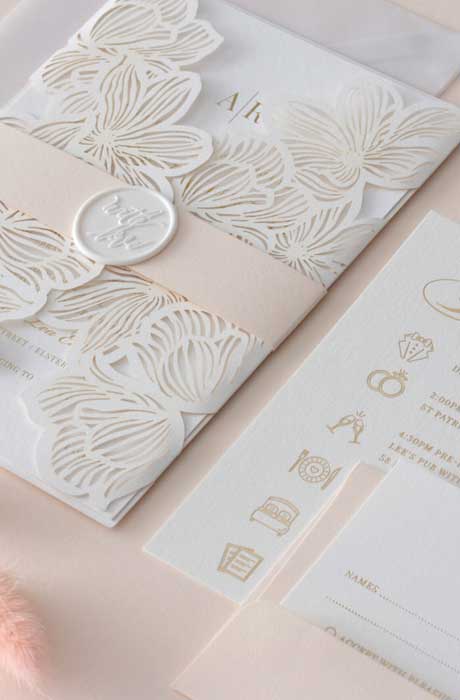 A pink and white wedding invitation suite with a stamped gold monogram in the center. 