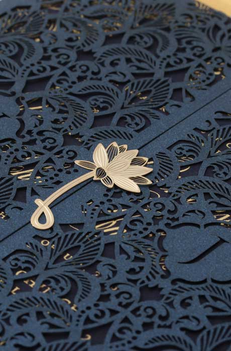 A closeup of a bi-fold blue and gold wedding  invitation with a gold flower stamp in the center. 