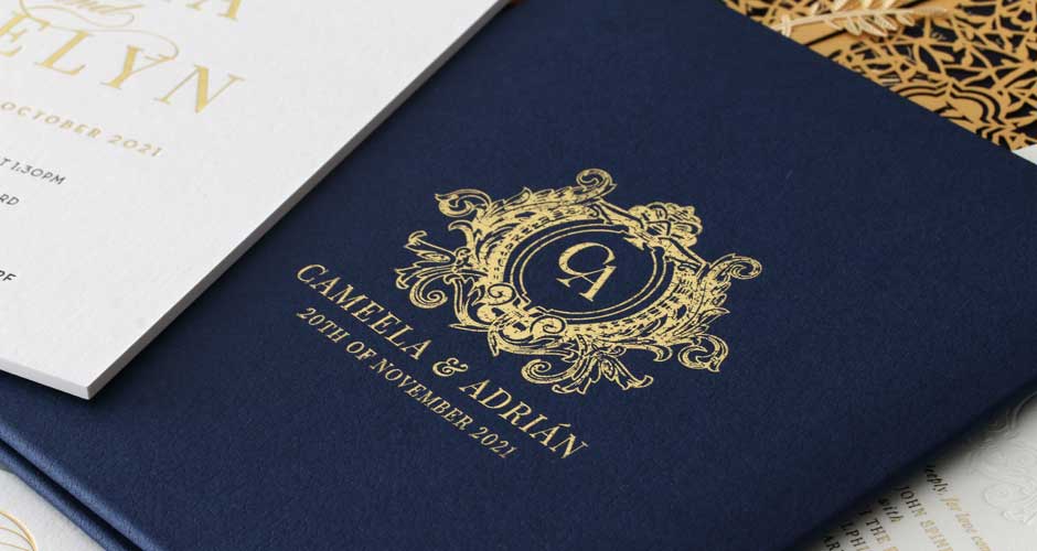 A navy blue invitation book with monogram gold wording on the front panel of invite. 