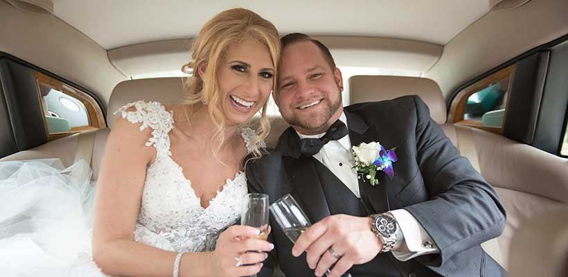 Bride and Groom holding champagne glasses inside their limousine.