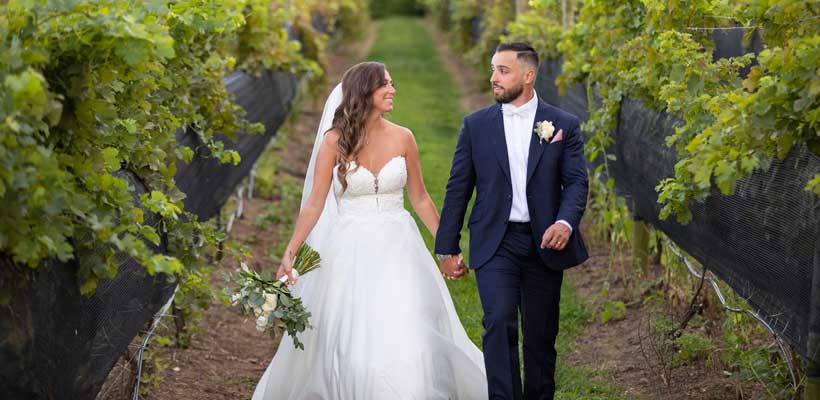 Bride and Groom walking through a vineyard holding hands. 
