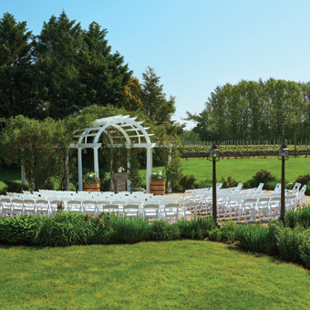 Full view of a white wedding arch and chairs surrounded by greenery. 