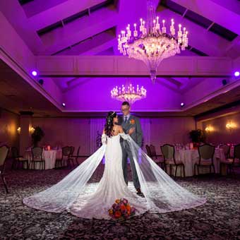 Bride and groom dancing in ballroom with purple uplighting. 
